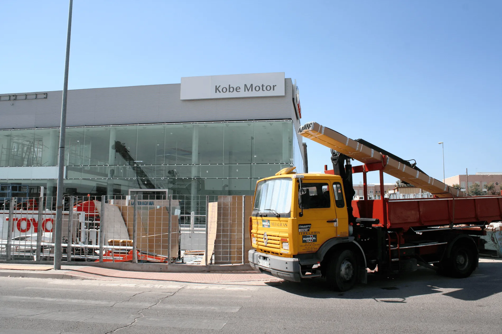 Fachada en construcción del concesionario Kobe Motor, con materiales de aluminio y vidrio.