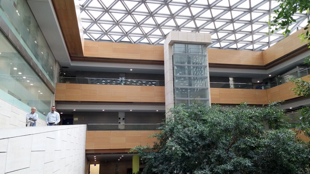 Interior de edificio con estructura de vidrio y techo geométrico de aluminio, diseño moderno en Madrid.
