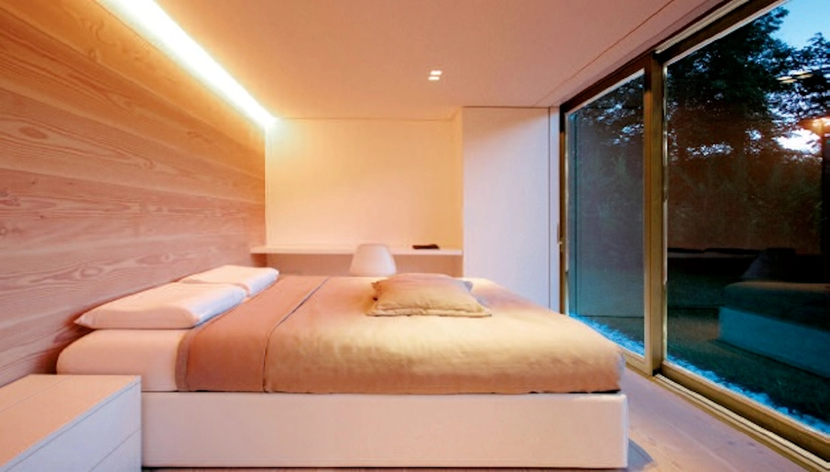 Dormitorio contemporáneo con puertas correderas de aluminio y cristal, iluminación ambiental.